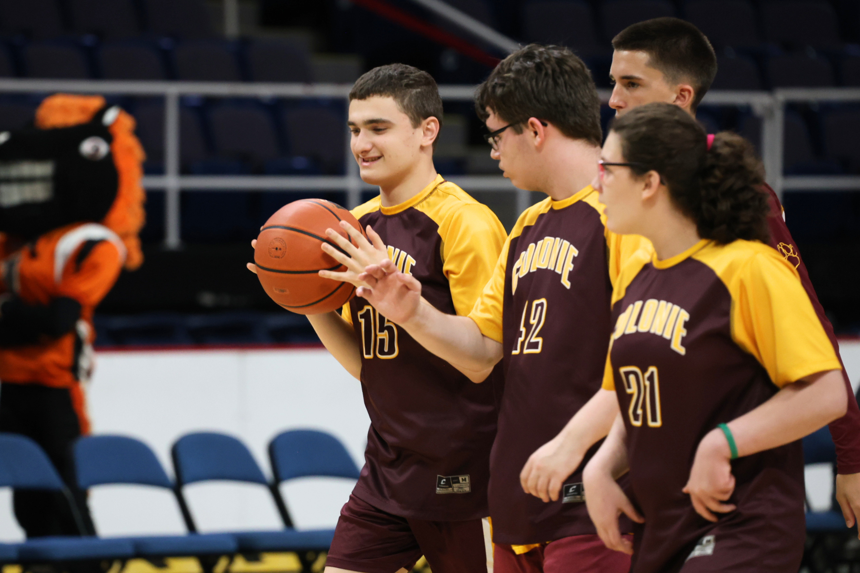 A group of basketball players in matching maroon and gold uniforms stand together on an indoor court.